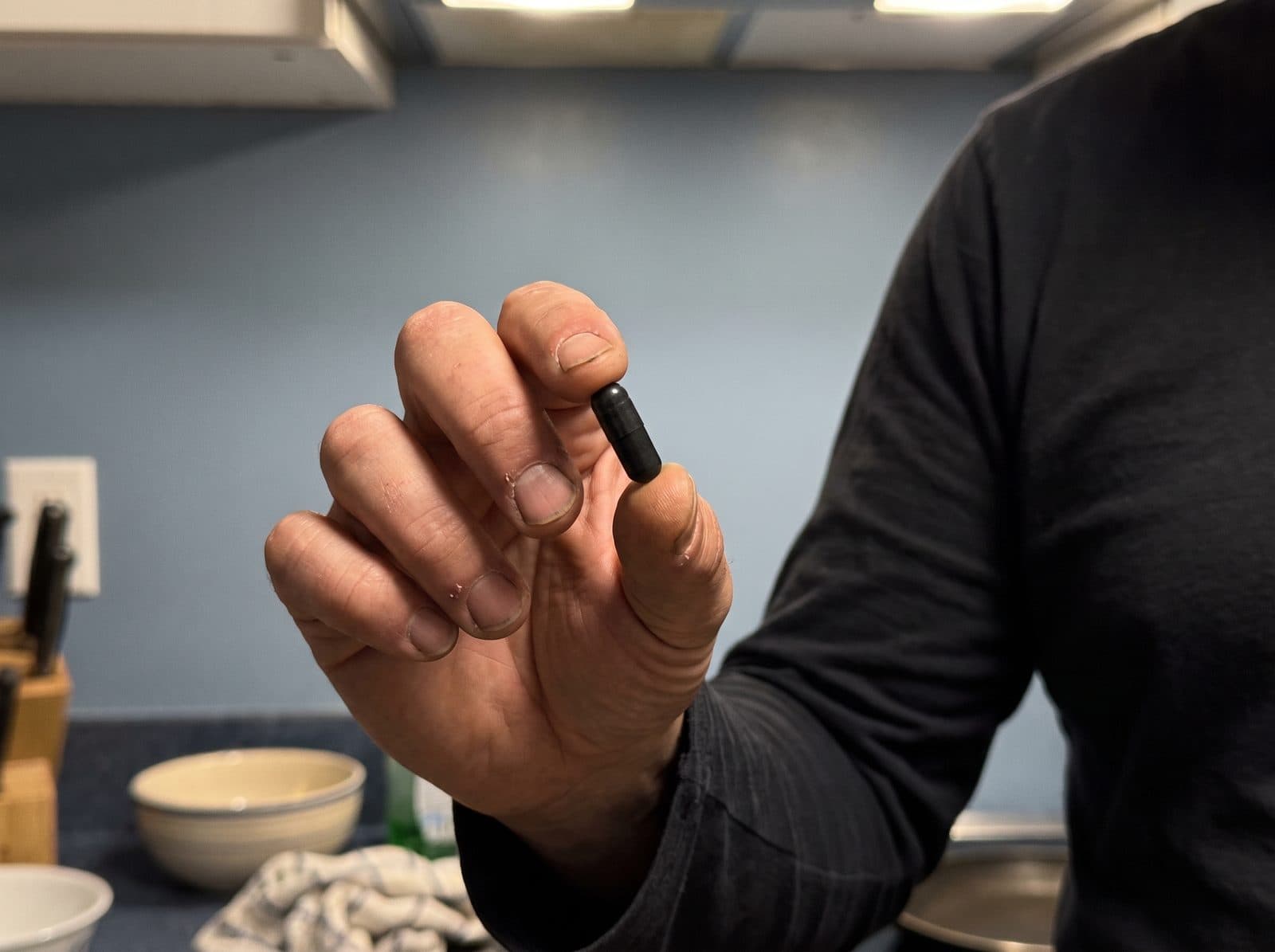 Une gélule noire de charbon actif tenue entre deux doigts